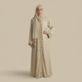 Woman wearing a beige abaya with intricate patterns on a beige background